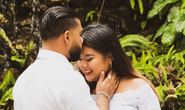 A married couple posing facing each other with the husband kissing her forehead